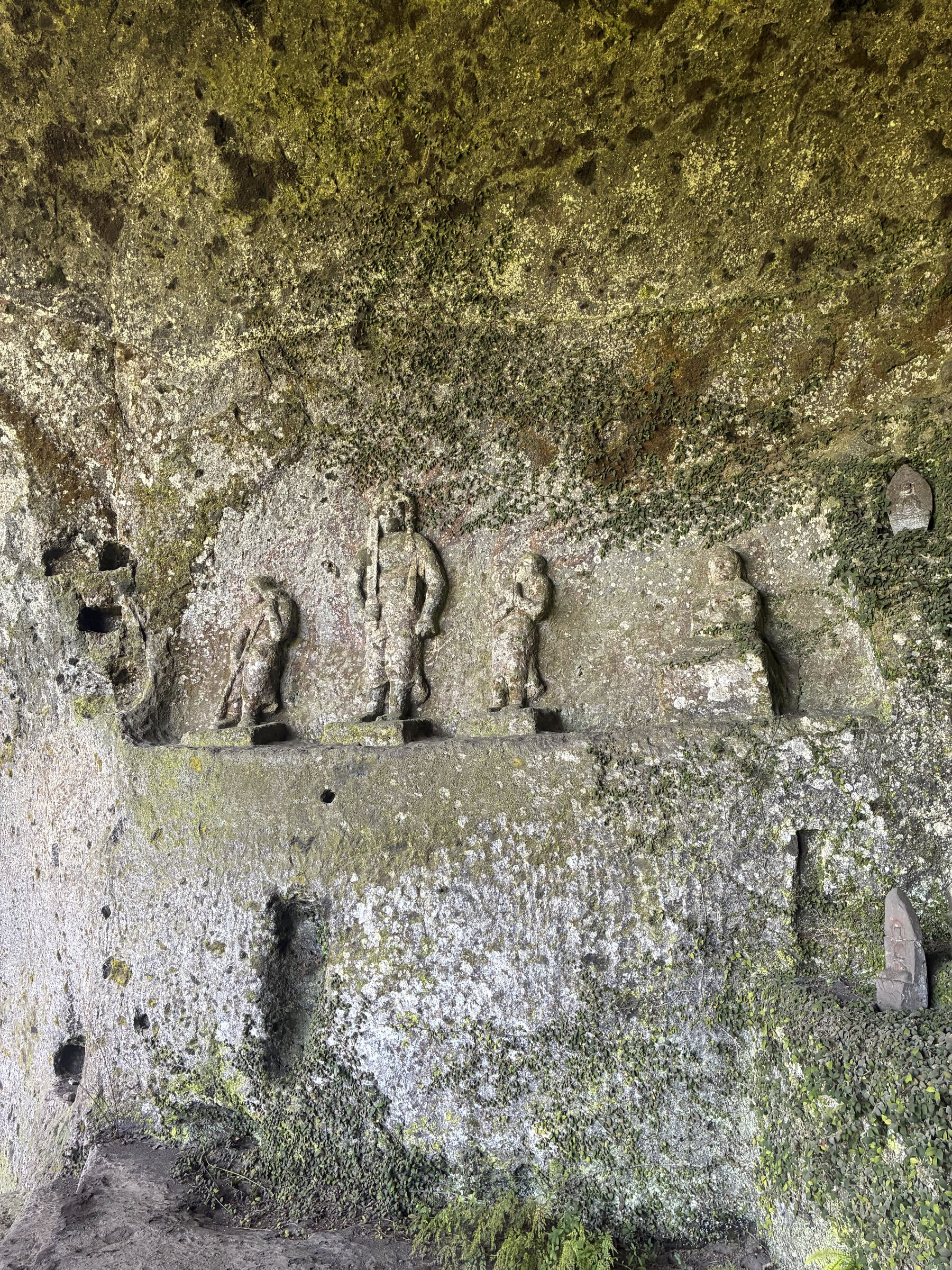 Weathered stone figures carved into the rock wall at Fukoji