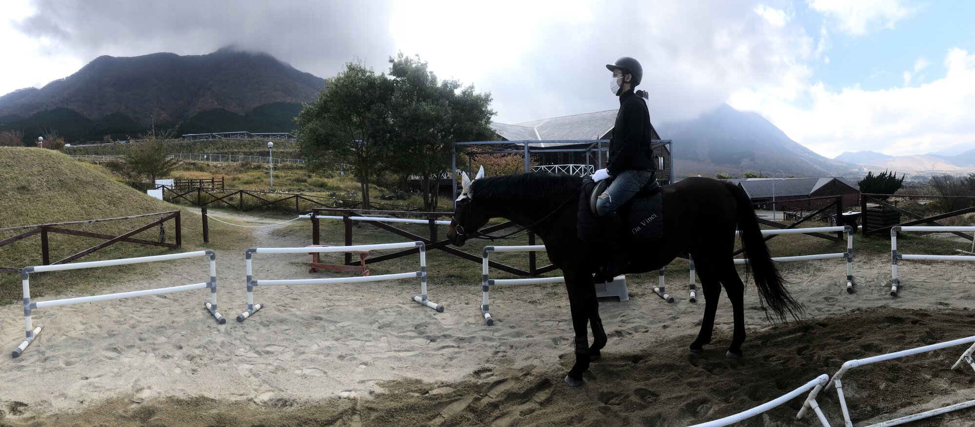 Panoramic view of the outdoor riding arena at Crane Yufuin with Mt. Yufu behind the practice jump course