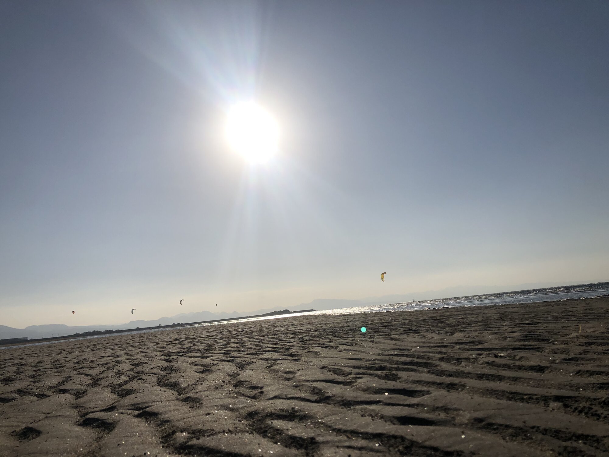 Low-angle view across the sand at Matama Coast with kites visible in the distance