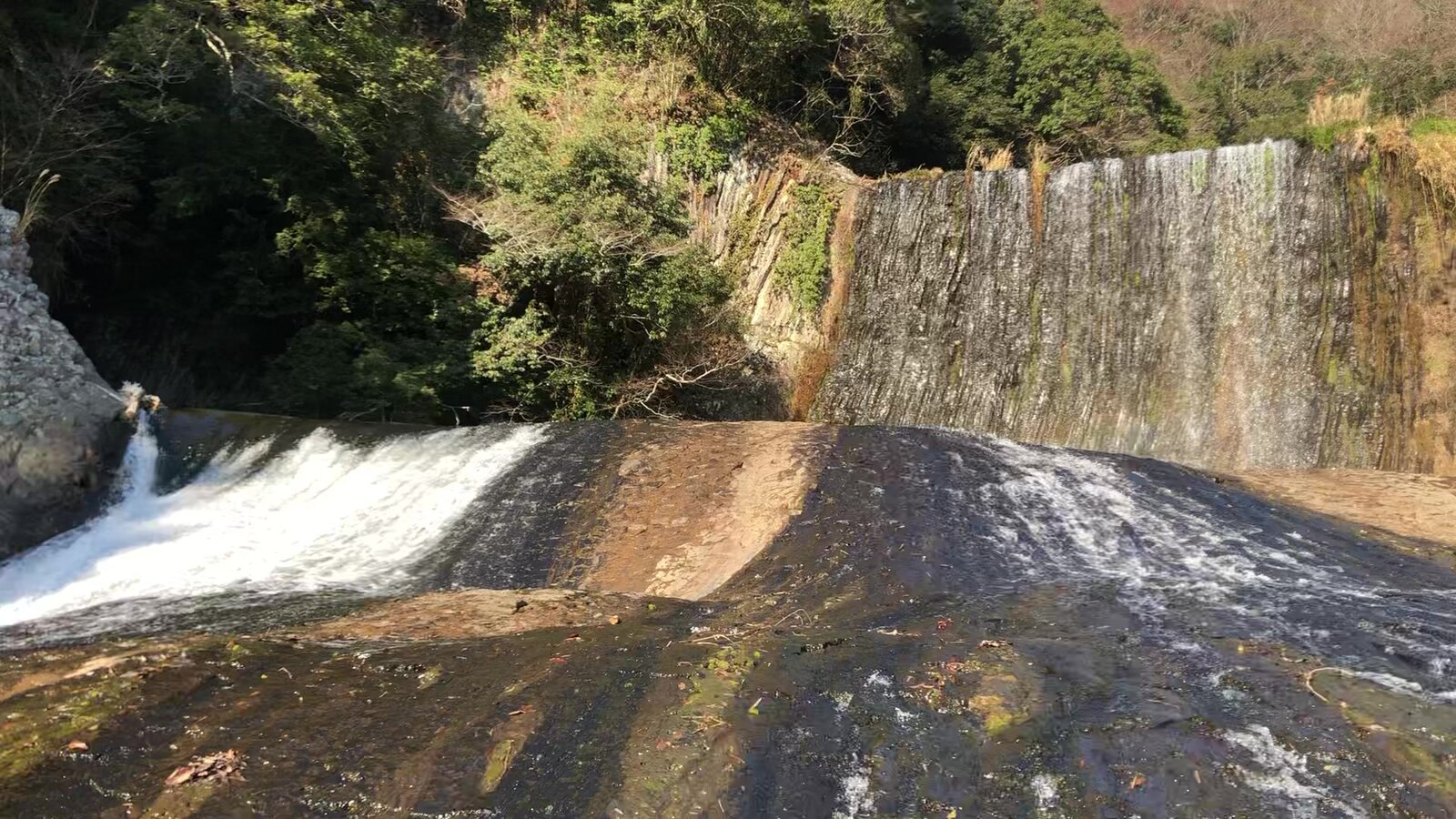 Side angle view of the full width of Ryumon Falls over the rock wall