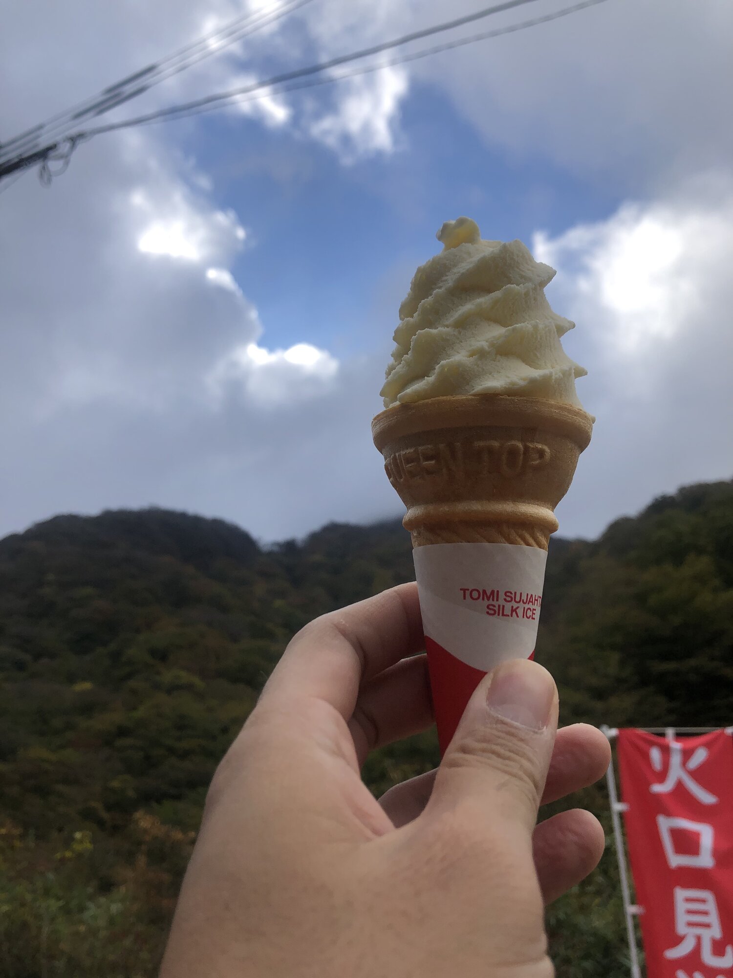 Soft-serve ice cream at Tsukahara Onsen with a crater-viewing banner in the background